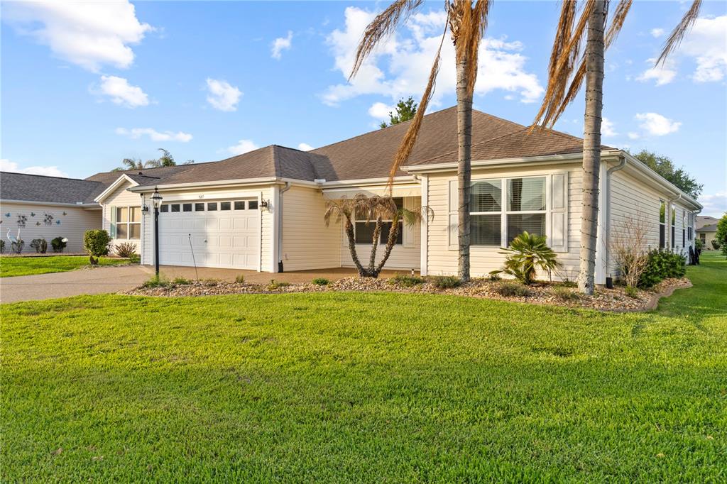 A single-story house with beige siding, a two-car garage, and palm trees in the yard — 589 SHERWOOD STREET, THE VILLAGES, FL