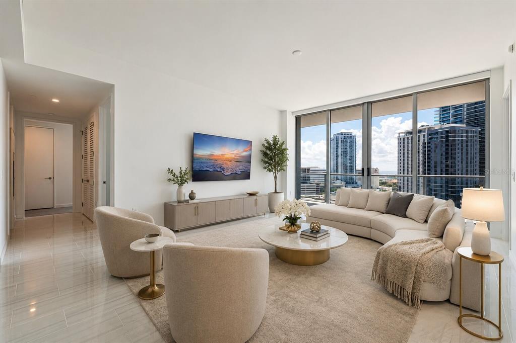 A modern living room features a curved sofa, two armchairs, a television, and floor-to-ceiling windows — 400 CENTRAL AVENUE UNIT 1105, ST PETERSBURG, FL