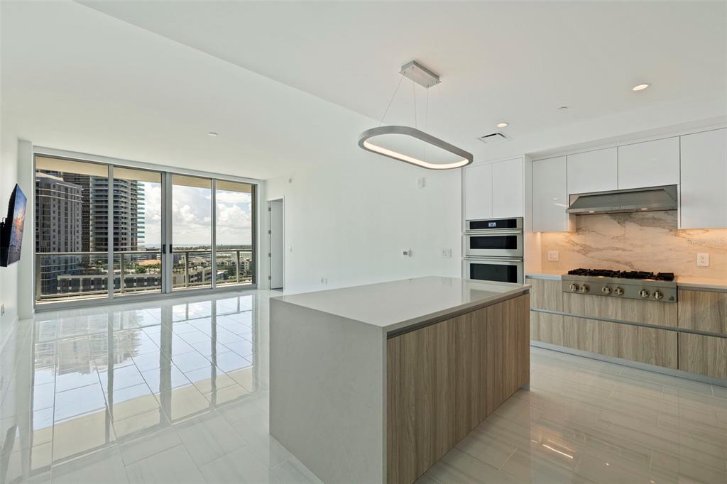 A modern kitchen with a wood-paneled island, white cabinetry, and floor-to-ceiling windows overlooking city buildings — 400 CENTRAL AVENUE UNIT 1105, ST PETERSBURG, FL