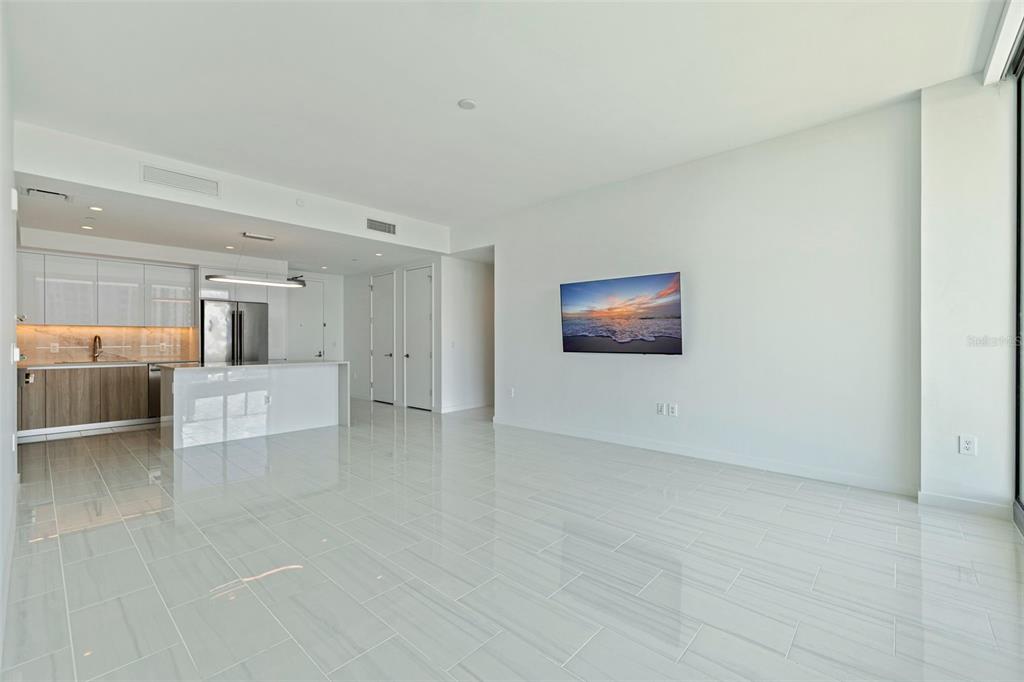 A modern, open-concept living room and kitchen with white tile floors and a wall-mounted television — 400 CENTRAL AVENUE UNIT 1105, ST PETERSBURG, FL