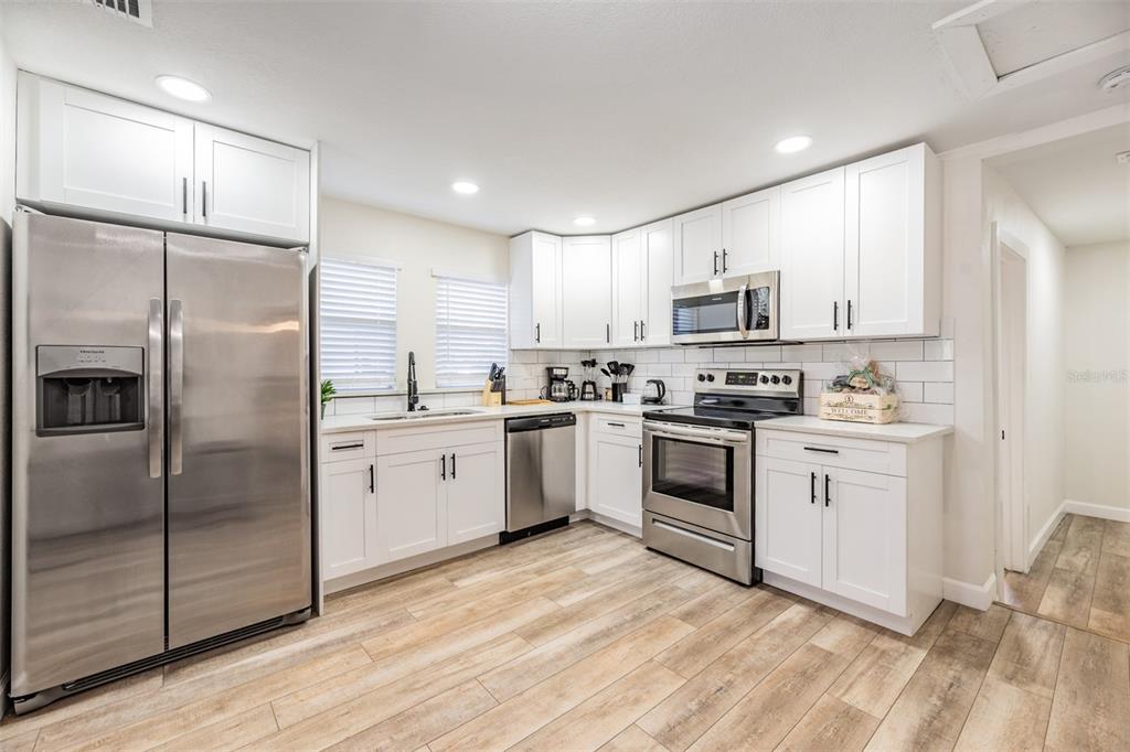 A kitchen features white cabinets, stainless steel appliances, a subway tile backsplash, and wood-look flooring — 4206 N 13TH STREET, TAMPA, FL