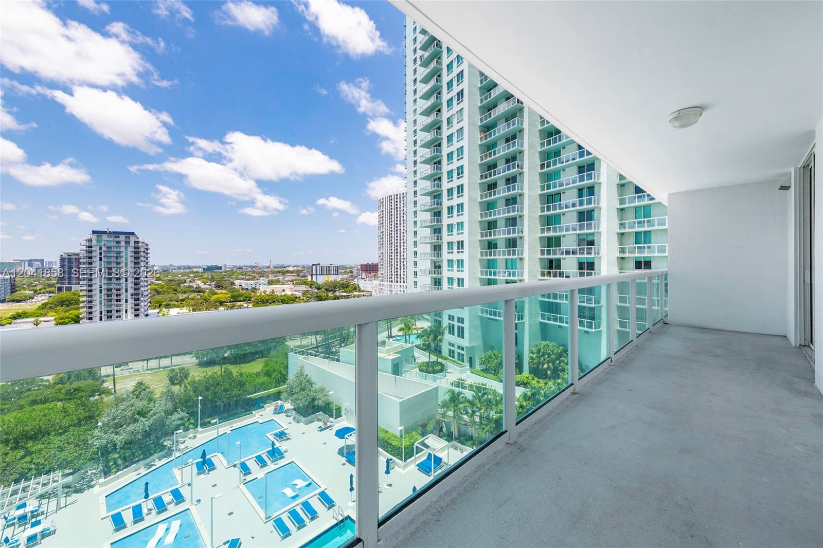 A balcony with a glass railing overlooks a swimming pool and city skyline — 1800 N Bayshore Dr # 1806, Miami FL 33132, MIAMI, FL