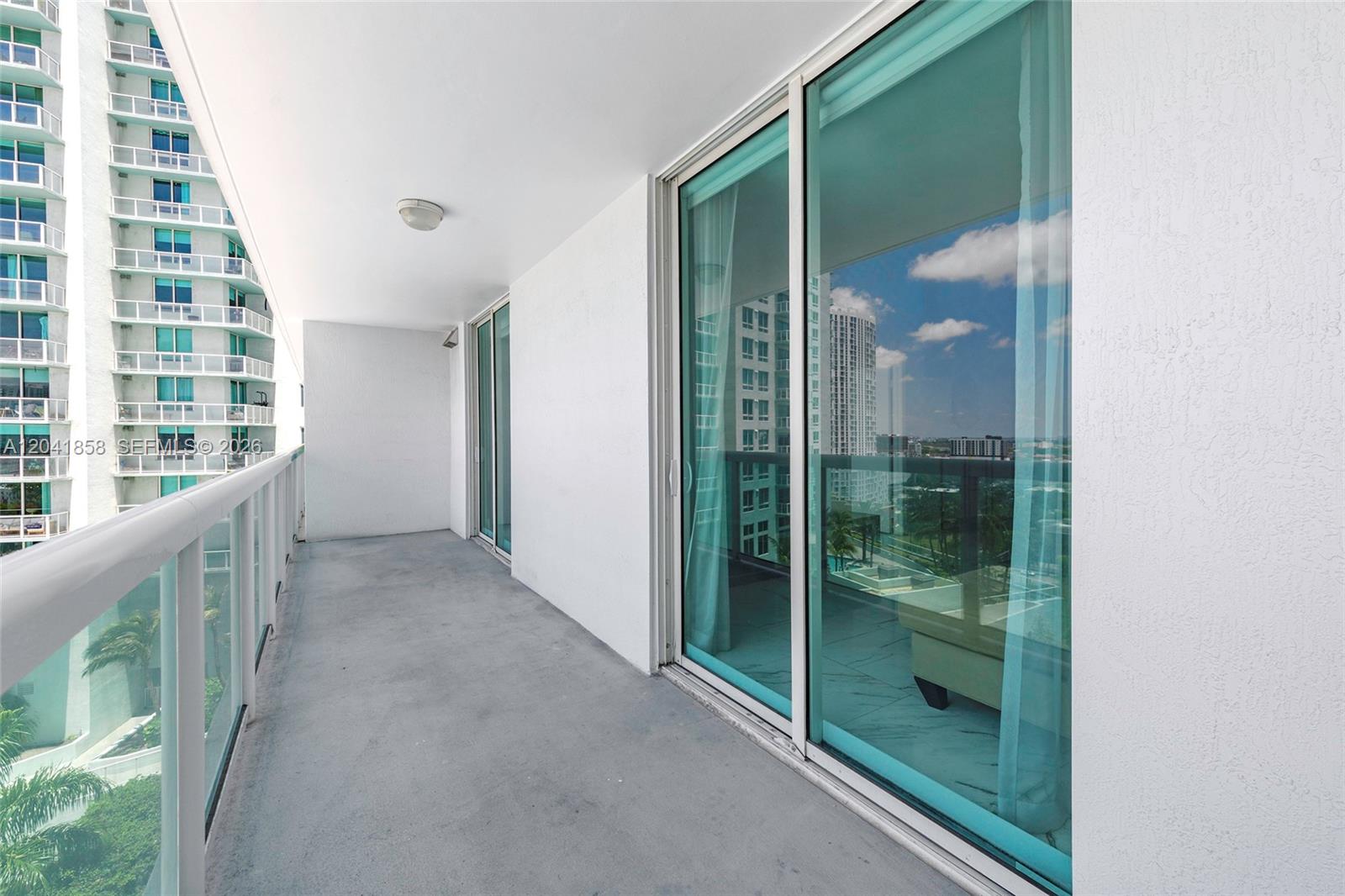 A balcony with a concrete floor, white walls, and sliding glass doors overlooking a city — 1800 N Bayshore Dr # 1806, Miami FL 33132, MIAMI, FL