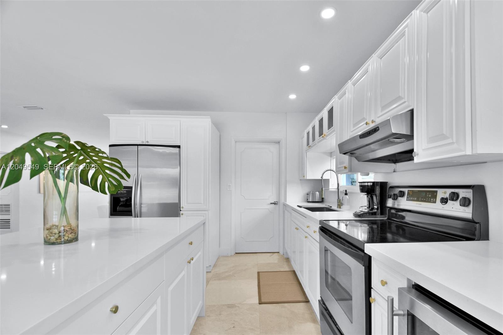 A modern kitchen features white cabinetry, stainless steel appliances, and a large white island — 2195 SW 25th Ter, Miami FL 33133, MIAMI, FL