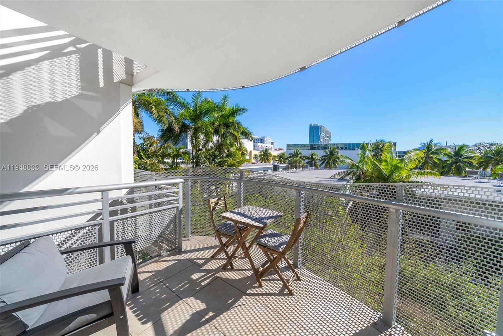 A balcony features a small table with two chairs, metal railings, and palm tree views — 2155 Washington Ct # 303, Miami Beach FL 33139, MIAMI BEACH, FL