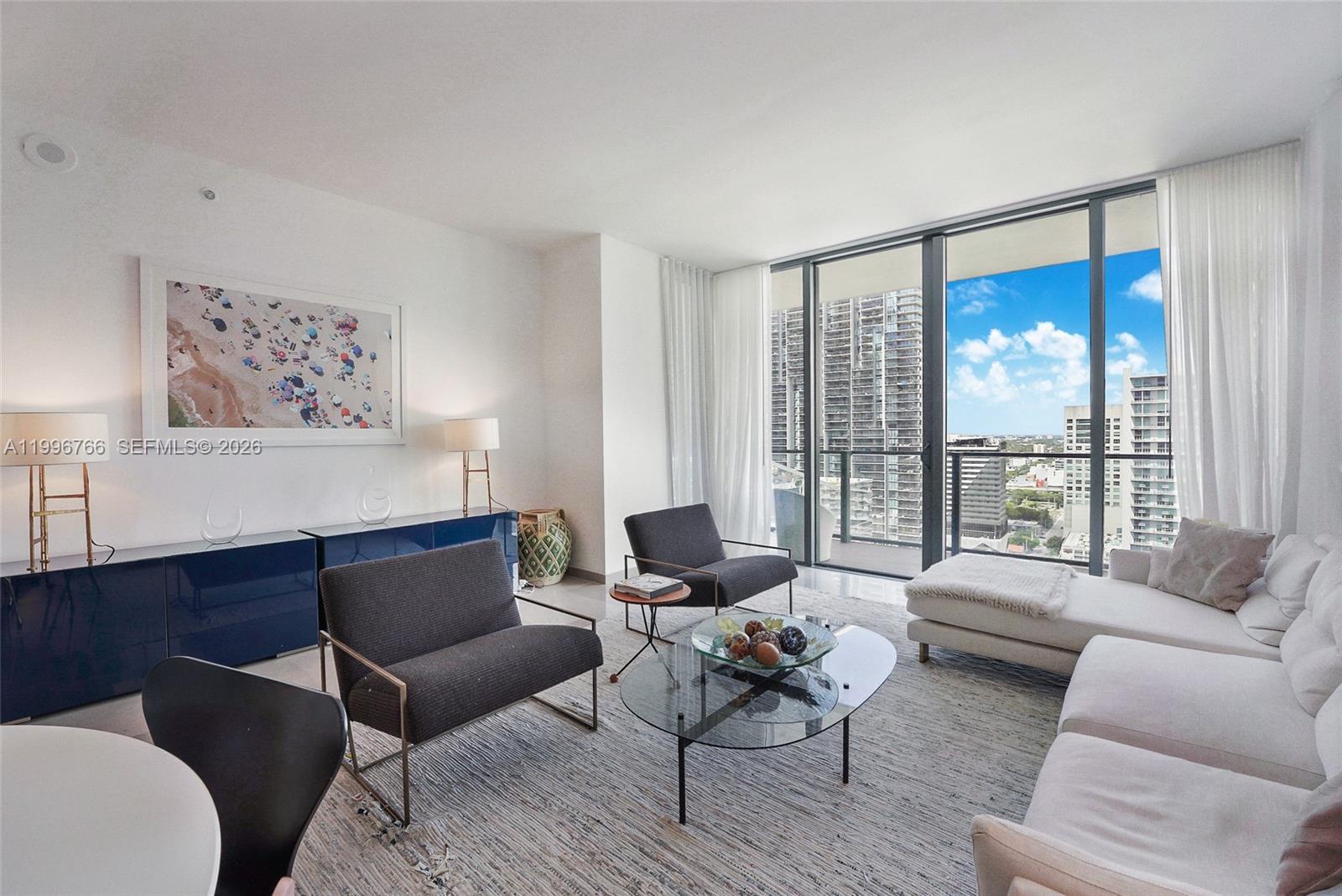 A modern living room features a glass coffee table, dark armchairs, and floor-to-ceiling windows — 68 SE 6th St # 2104, Miami FL 33131, MIAMI, FL