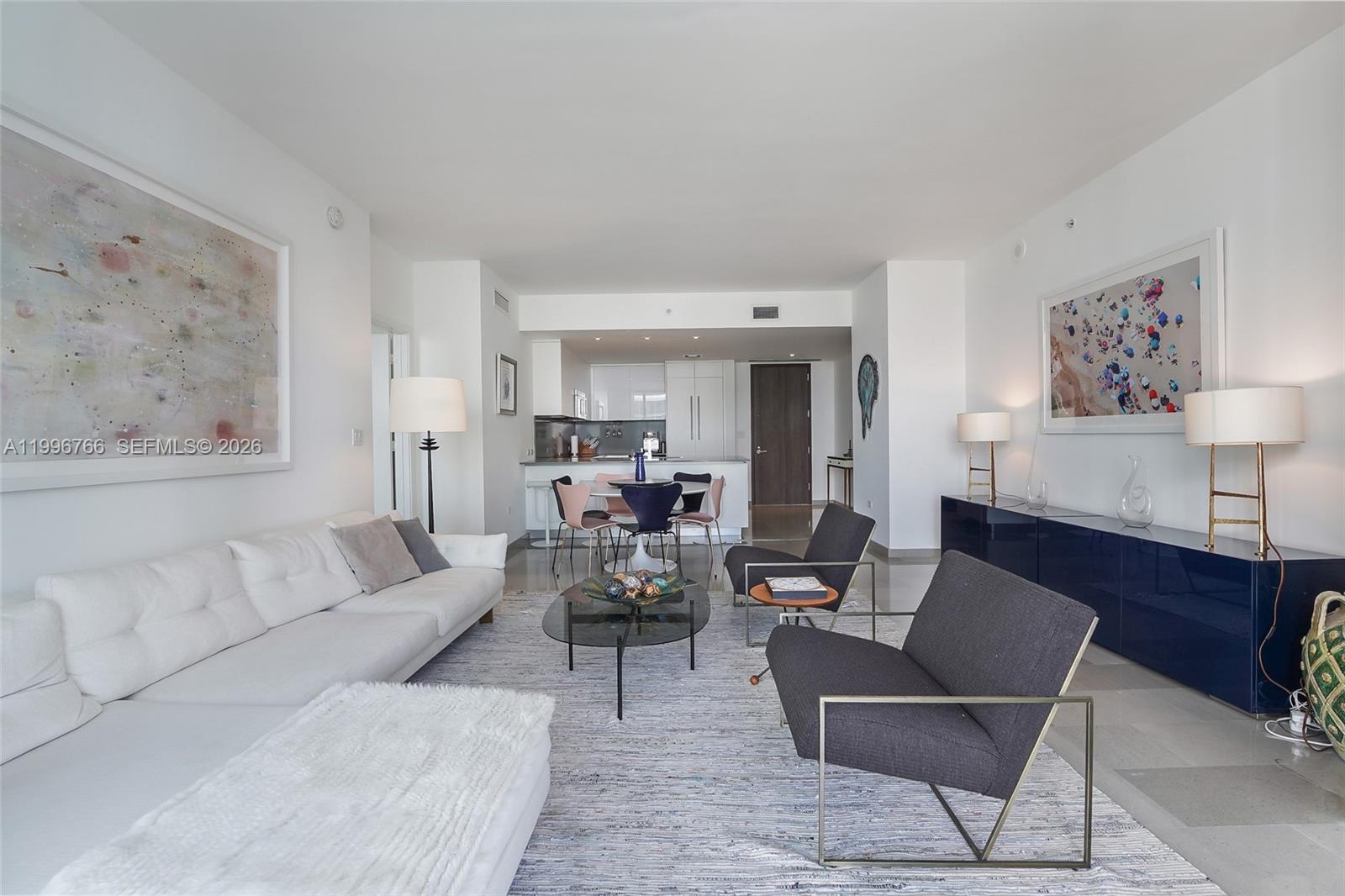 A modern living room features a white sofa, two dark armchairs, and an open kitchen — 68 SE 6th St # 2104, Miami FL 33131, MIAMI, FL