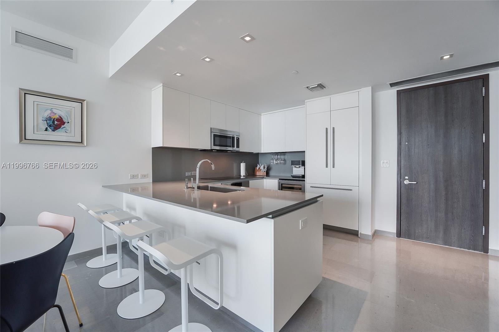 A modern kitchen features white cabinetry, a gray countertop island, and three white bar stools — 68 SE 6th St # 2104, Miami FL 33131, MIAMI, FL