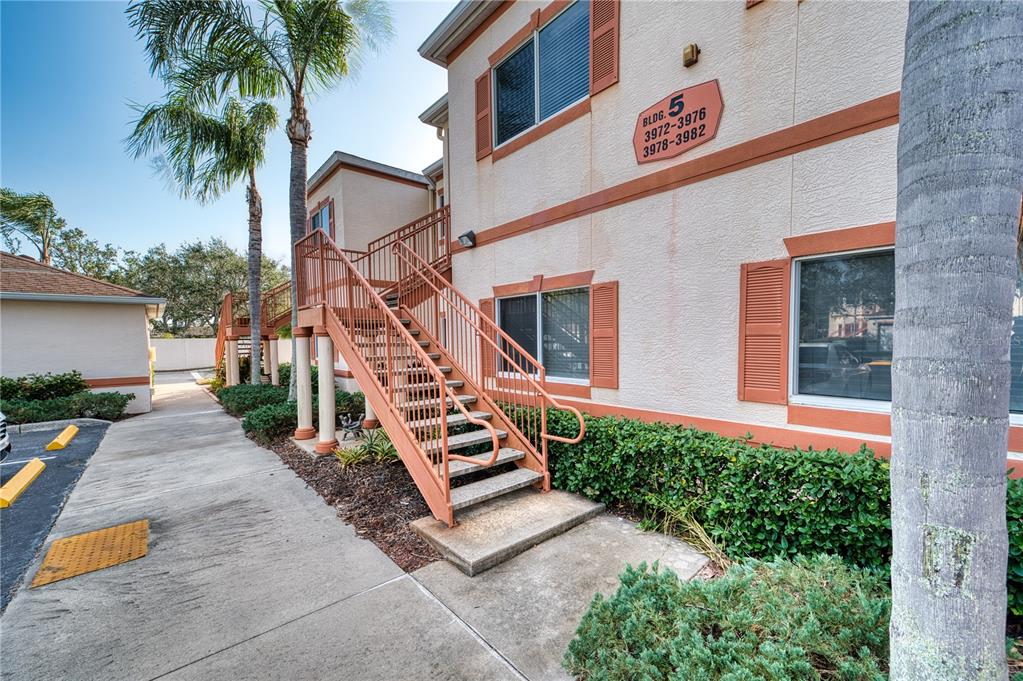 An exterior view of a two-story apartment building with metal stairs and palm trees — 3980 MEDITERRANEA CIRCLE UNIT 522, SARASOTA, FL