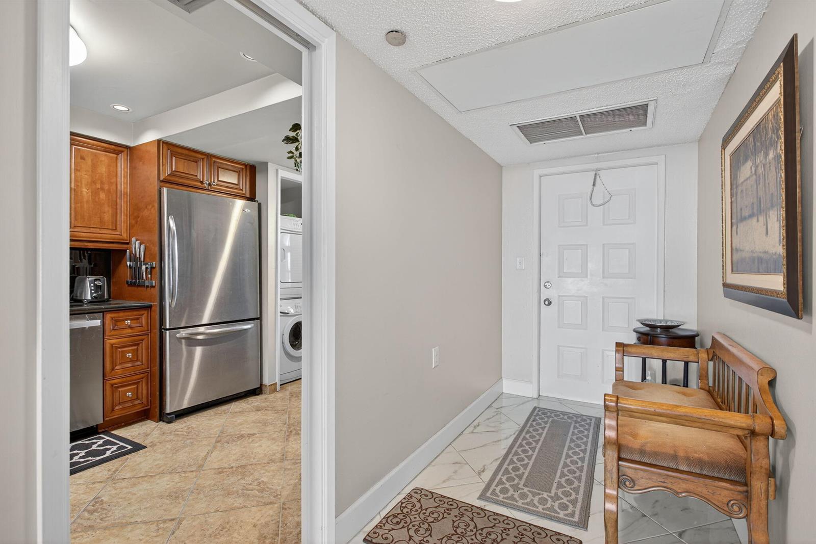 An entryway with a wooden bench leads into a kitchen featuring stainless steel appliances — 2900 N Course Drive # 905, Pompano Beach FL 33069, POMPANO BEACH, FL