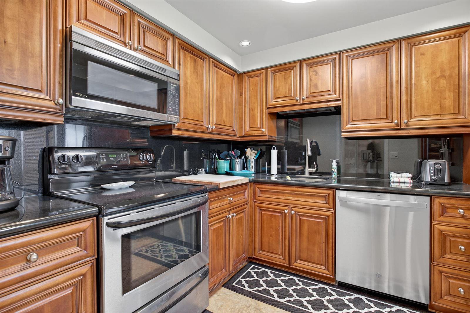 A kitchen features wood cabinets, stainless steel appliances, and black countertops — 2900 N Course Drive # 905, Pompano Beach FL 33069, POMPANO BEACH, FL