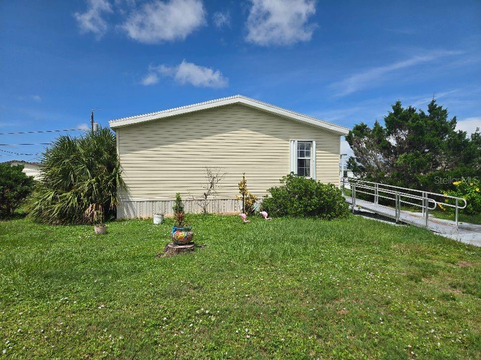 A light-colored mobile home with a metal wheelchair ramp sits on a grassy lot — 1366 FLAMINGO DRIVE, ENGLEWOOD, FL