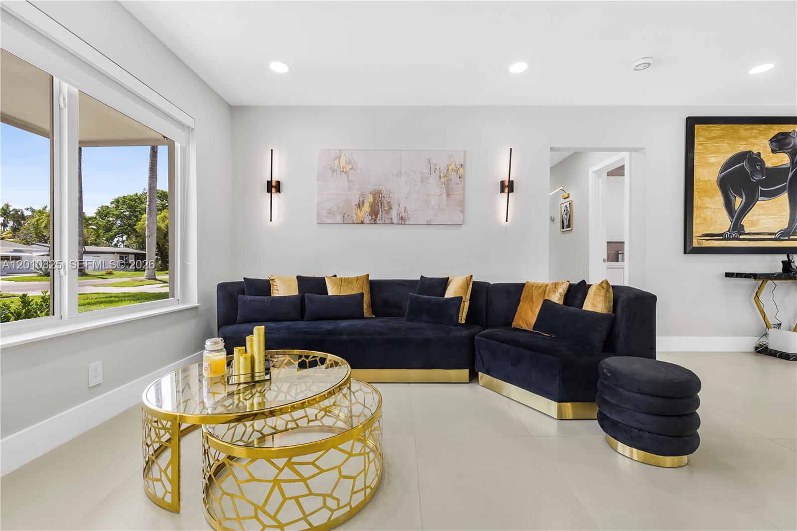 A living room features a navy blue sectional sofa, gold-accented coffee tables, and wall art — 1104 N 13th Ter, Hollywood FL 33019, HOLLYWOOD, FL