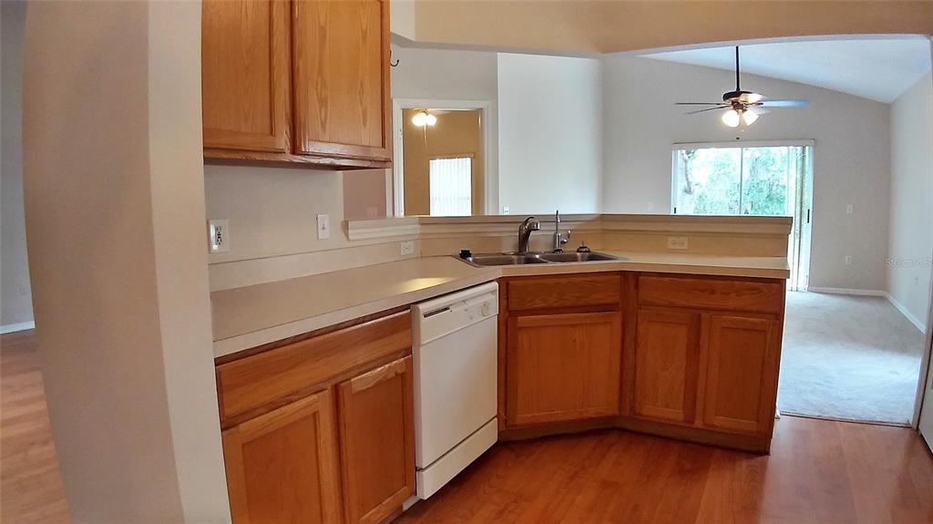 A kitchen features wood cabinets, a white dishwasher, a corner sink, and hardwood flooring — 3842 STONEFIELD DRIVE, ORLANDO, FL