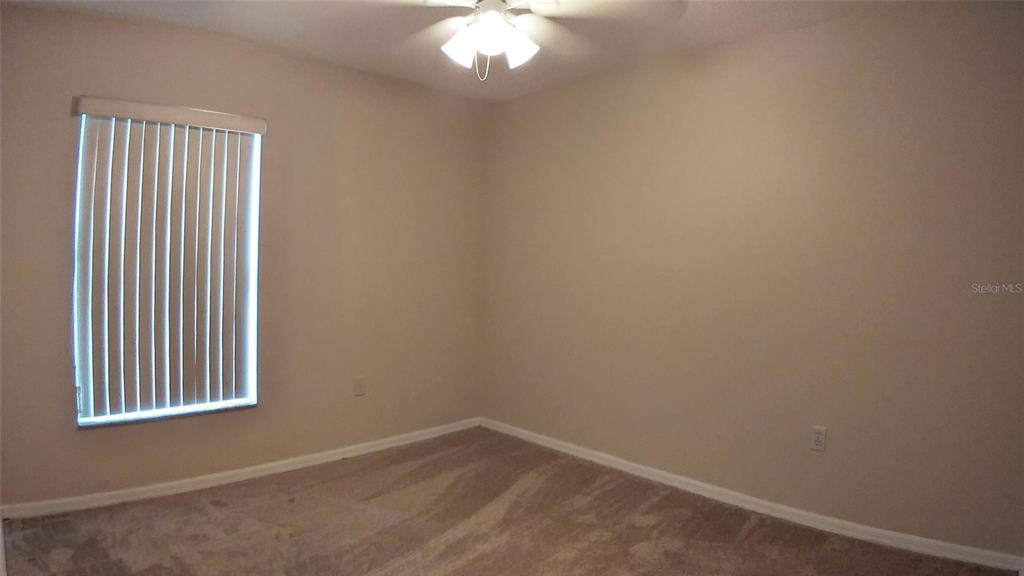 An empty bedroom features beige walls, tan carpeting, and a window with vertical blinds — 3842 STONEFIELD DRIVE, ORLANDO, FL