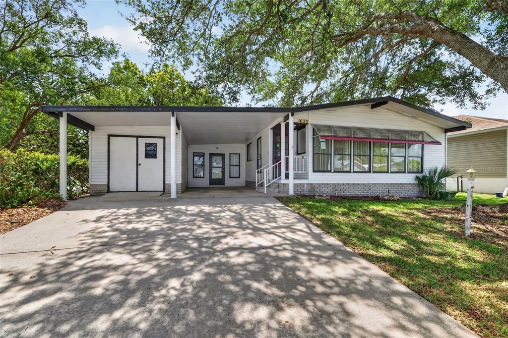 A single-story house with a carport, white siding, and a concrete driveway under large trees — 1625 HILTON HEAD BOULEVARD, LADY LAKE, FL