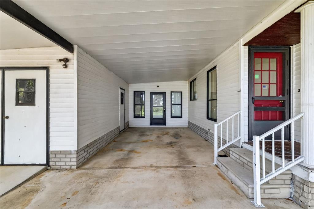 A concrete carport features white siding, a red front door, and several windows — 1625 HILTON HEAD BOULEVARD, LADY LAKE, FL