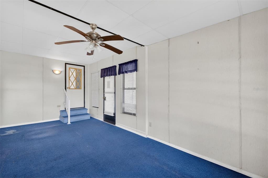A sunroom features blue carpeting, a ceiling fan, and a door leading to raised steps — 1625 HILTON HEAD BOULEVARD, LADY LAKE, FL