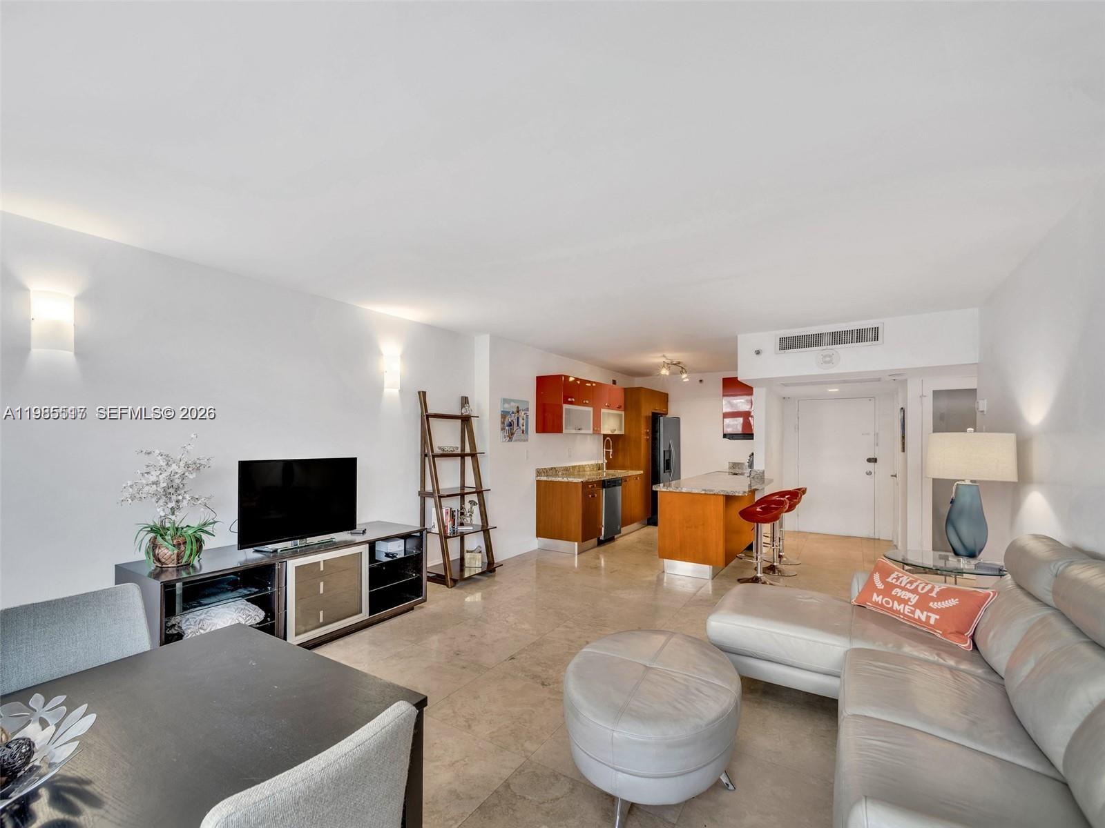 An open-concept living area features a kitchen with wood cabinets, tile floors, and a sectional sofa — 100 Lincoln Rd # 308, Miami Beach FL 33139, MIAMI BEACH, FL