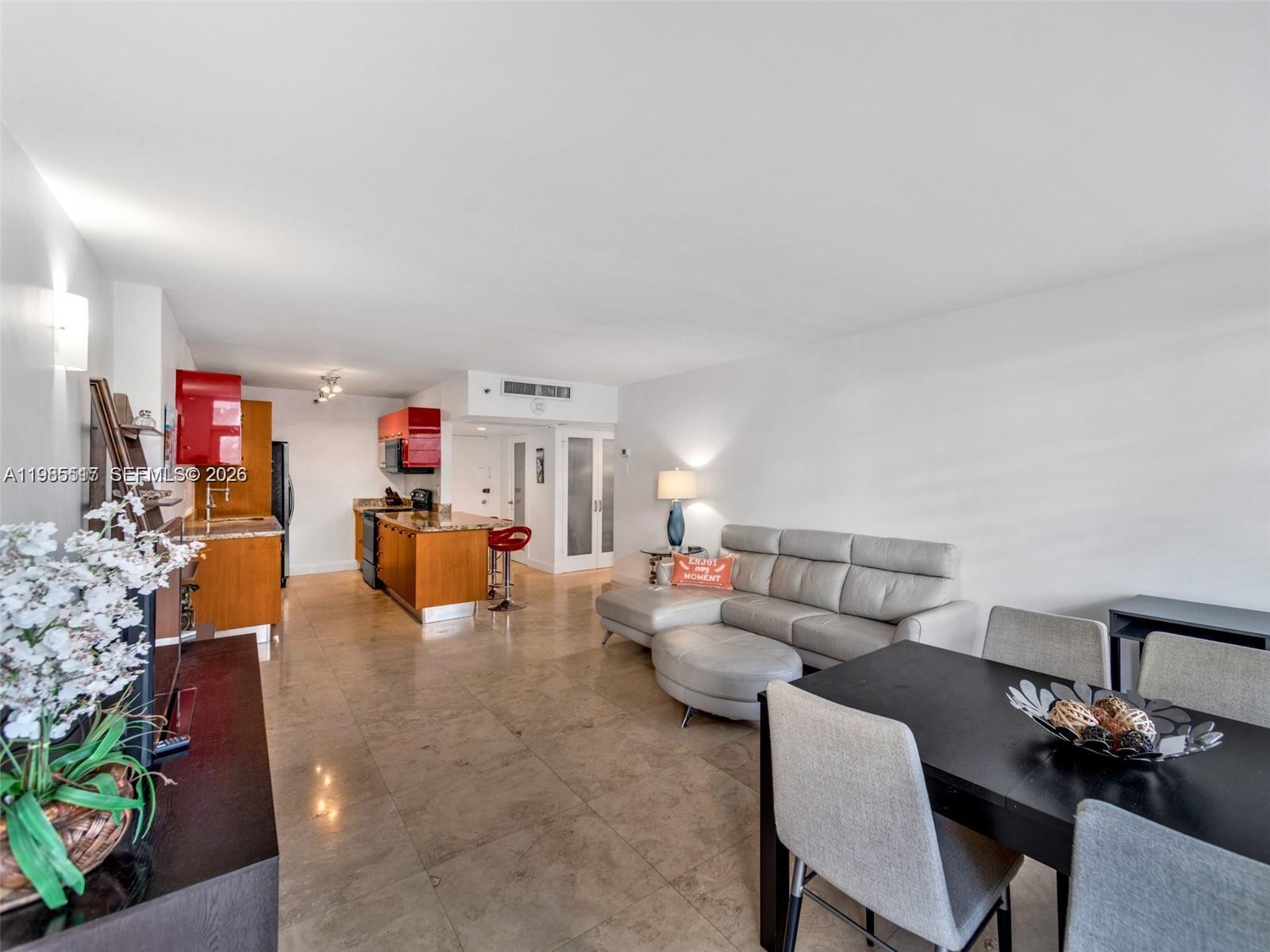 An open-concept living and dining area features tile flooring, a kitchen with red cabinets, and furniture — 100 Lincoln Rd # 308, Miami Beach FL 33139, MIAMI BEACH, FL