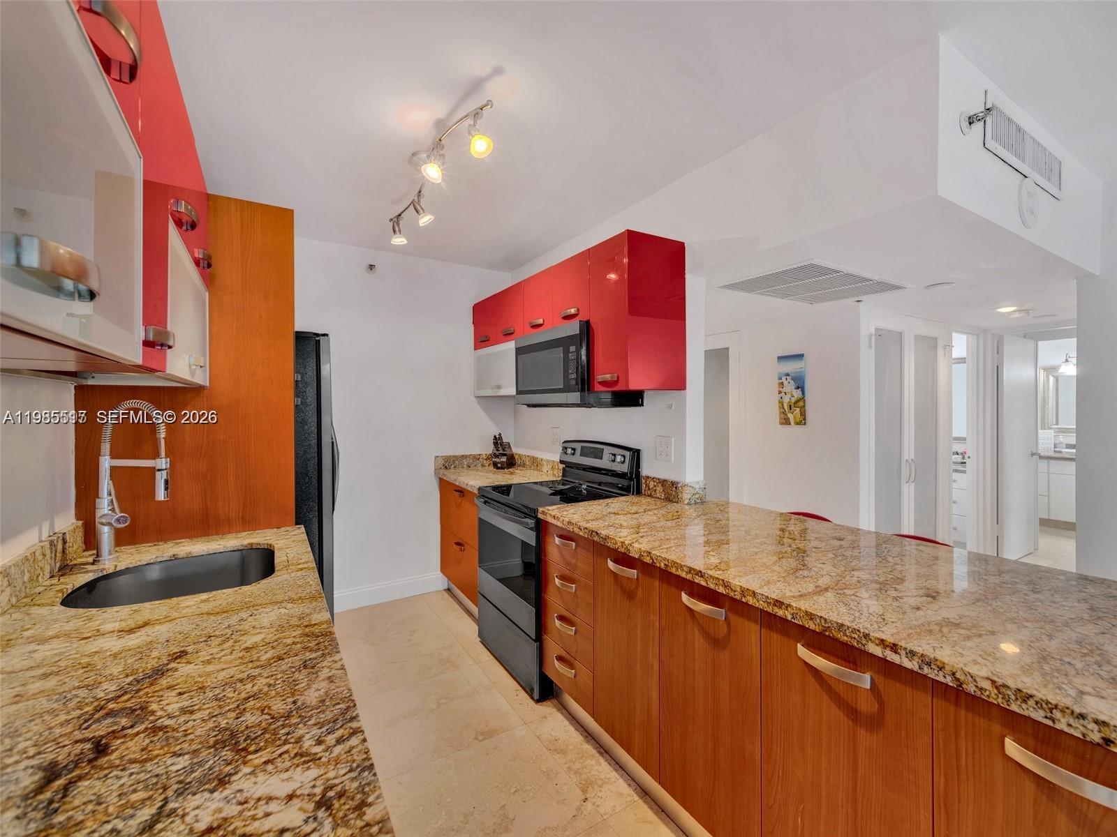 A kitchen features wood-toned lower cabinets, red upper cabinets, and granite countertops — 100 Lincoln Rd # 308, Miami Beach FL 33139, MIAMI BEACH, FL