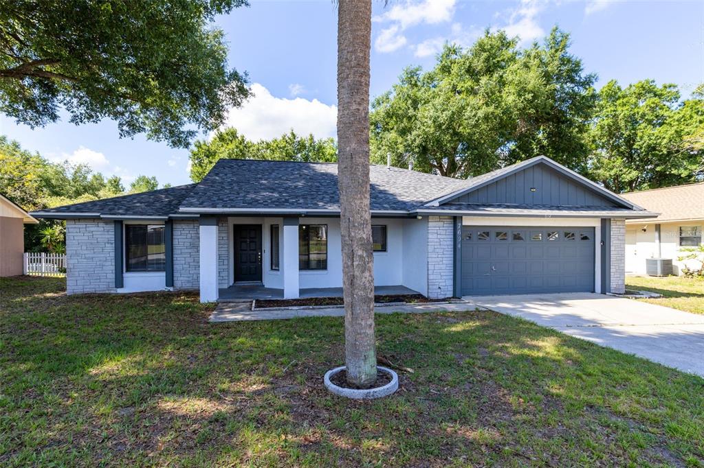 A single-story house with a gray garage, stone accents, and a large tree in front — 7694 INDIAN RIDGE TRAIL S, KISSIMMEE, FL