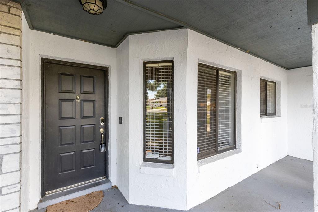 A white exterior wall features a dark front door and three windows under a porch — 7694 INDIAN RIDGE TRAIL S, KISSIMMEE, FL