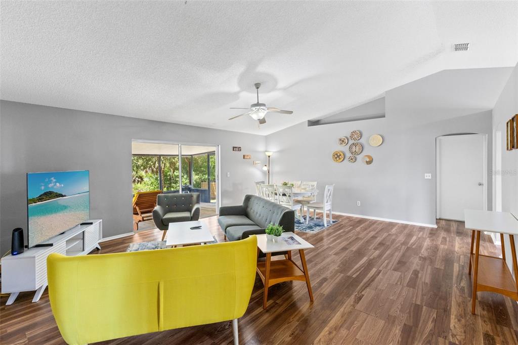 A living and dining area with gray walls, wood-look flooring, and a yellow sofa — 7694 INDIAN RIDGE TRAIL S, KISSIMMEE, FL