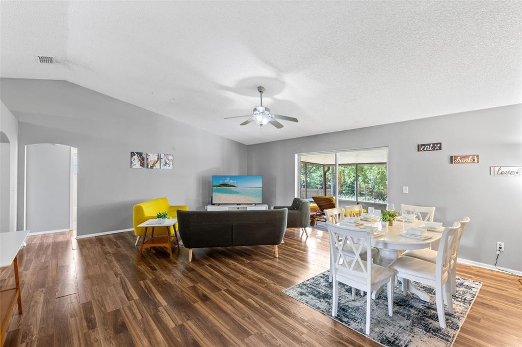 A living and dining area features wood-look flooring, a vaulted ceiling, and a sliding glass door — 7694 INDIAN RIDGE TRAIL S, KISSIMMEE, FL