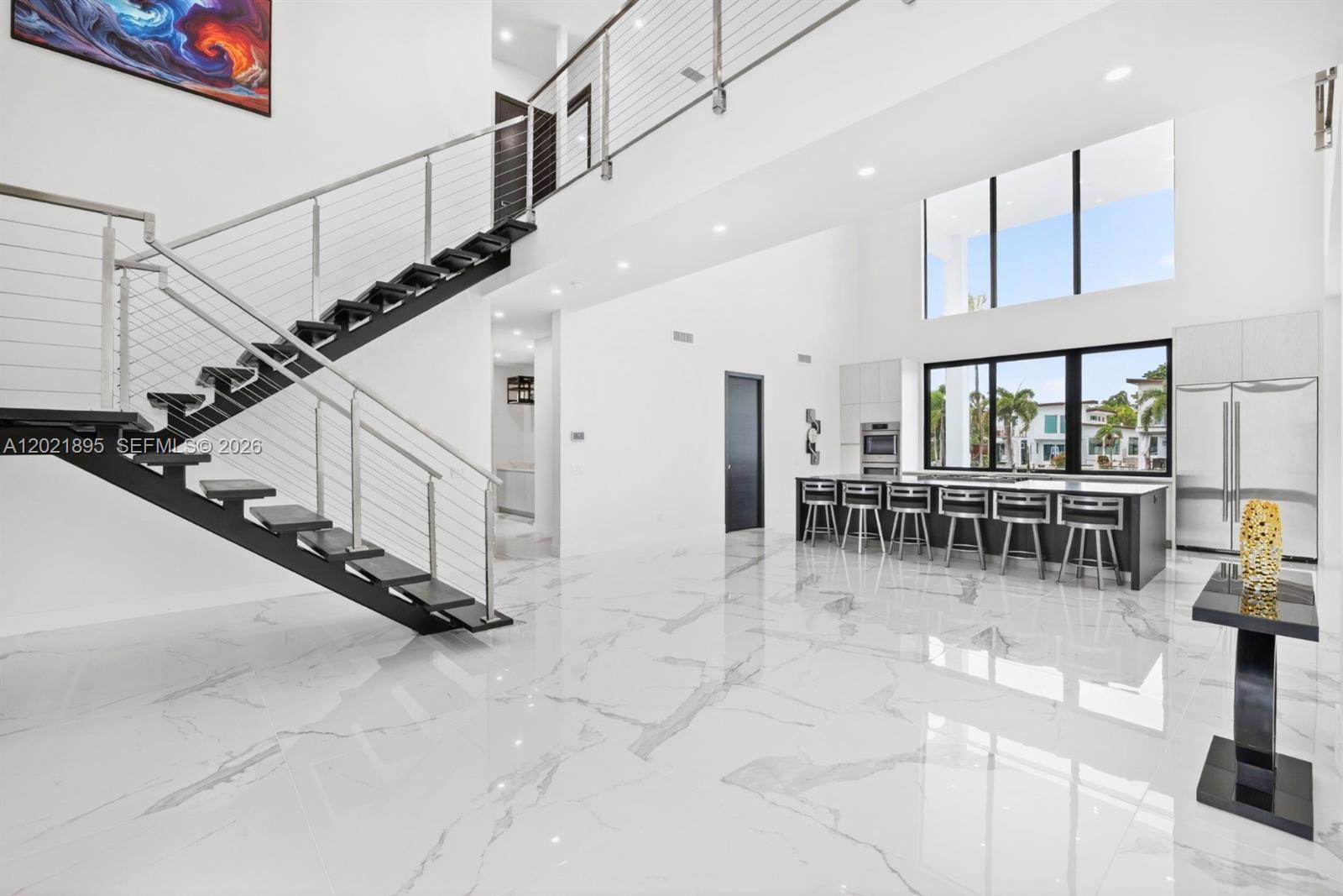 A modern, open-concept kitchen and living area features white marble floors and a floating staircase — 2751 NE 22nd Ct, Pompano Beach FL 33062, POMPANO BEACH, FL