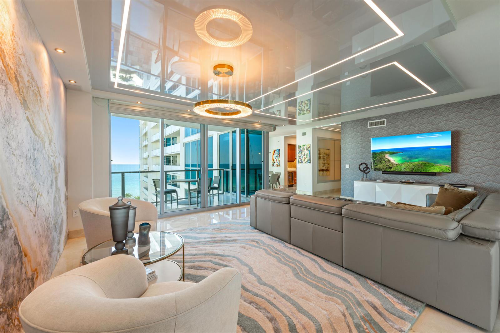 A modern living room features a grey sectional, two armchairs, and a reflective ceiling — 3101 S Ocean Drive # 901, Hollywood FL 33019, HOLLYWOOD, FL