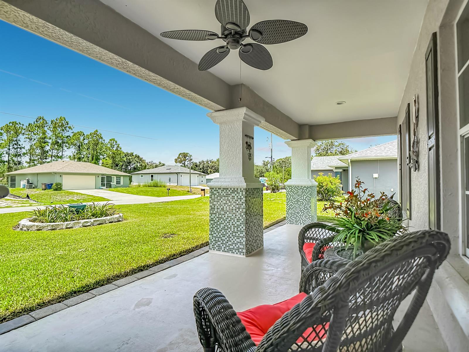 A covered porch features wicker chairs with red cushions, tiled columns, and a ceiling fan — 2610 53rd Street W, Lehigh Acres FL 33971, LEHIGH ACRES, FL