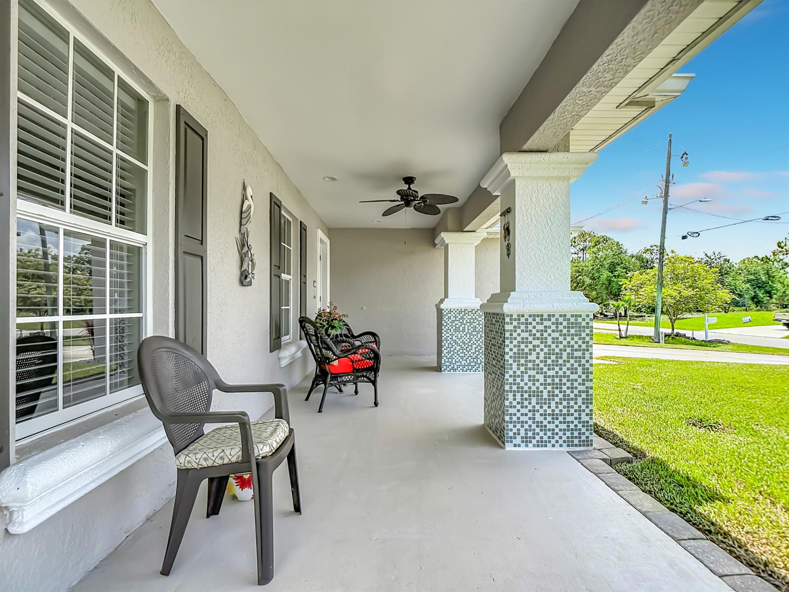 A covered front porch features tiled columns, a ceiling fan, and outdoor seating — 2610 53rd Street W, Lehigh Acres FL 33971, LEHIGH ACRES, FL