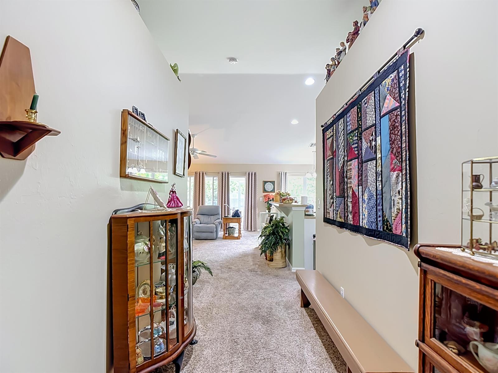 A hallway with a curio cabinet and wall quilt leads into an open living area — 2610 53rd Street W, Lehigh Acres FL 33971, LEHIGH ACRES, FL