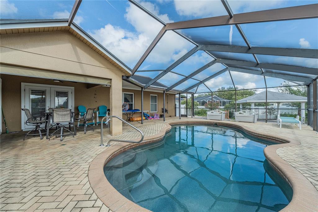 A screened-in patio features a kidney-shaped swimming pool and brick pavers under a metal frame — 205 THOMAS COURT, WINTER HAVEN, FL