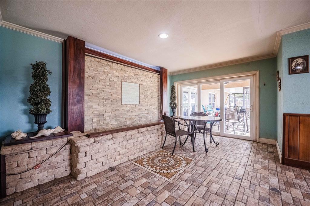 A room features a stone accent wall, tiled flooring, and a dining set near sliding doors — 205 THOMAS COURT, WINTER HAVEN, FL