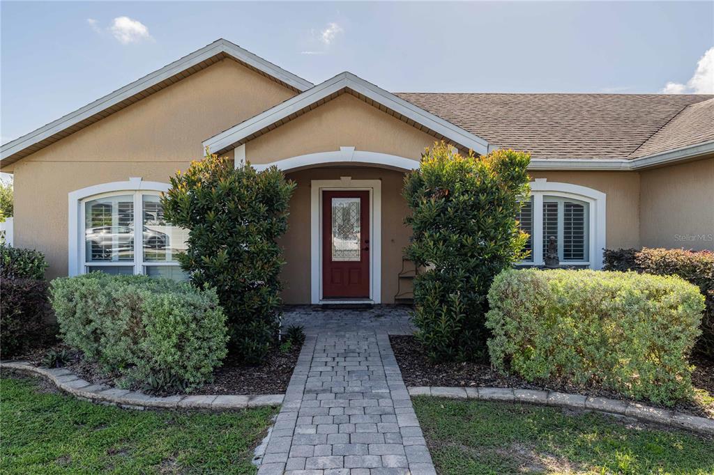 A tan house features a red front door, a paver walkway, and manicured landscaping — 205 THOMAS COURT, WINTER HAVEN, FL