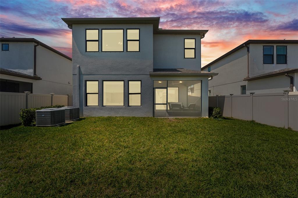 The rear exterior of a two-story house features a screened-in patio and a grassy yard — 4790 TRAMANTO LANE, WESLEY CHAPEL, FL