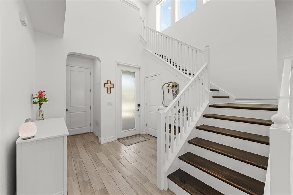 A bright entryway features a white staircase with dark wood treads and light wood flooring — 4790 TRAMANTO LANE, WESLEY CHAPEL, FL