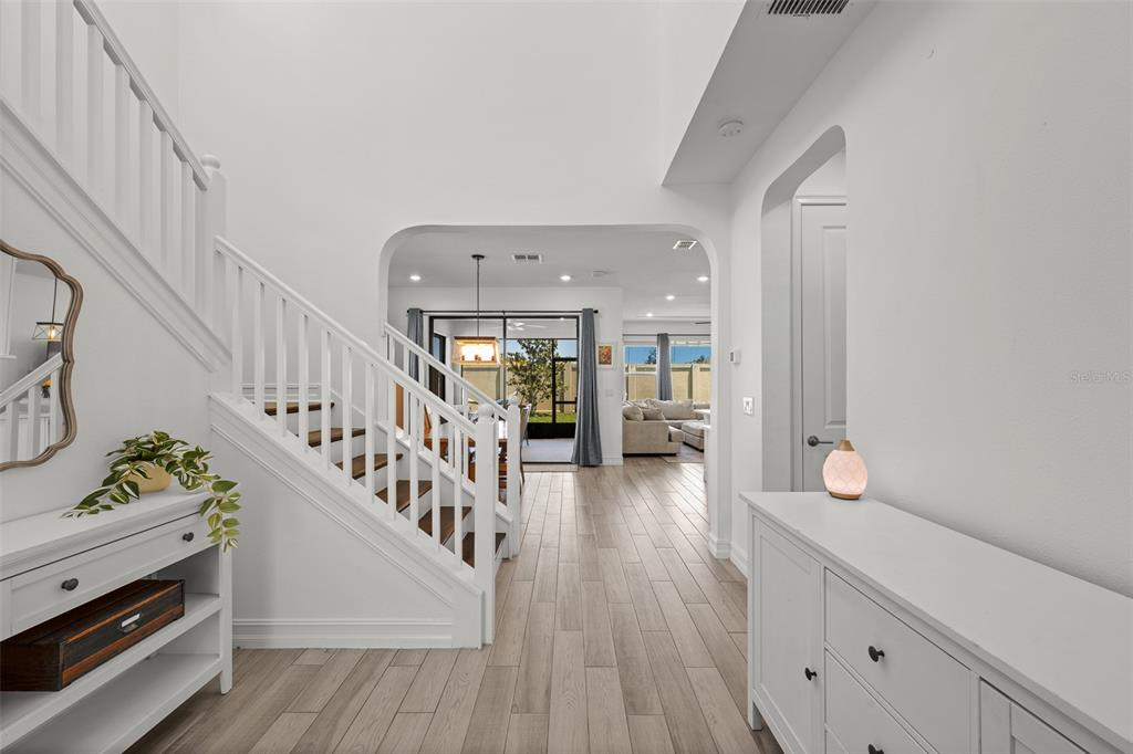 A bright entryway features white walls, wood-look tile flooring, a staircase, and an open floor plan — 4790 TRAMANTO LANE, WESLEY CHAPEL, FL