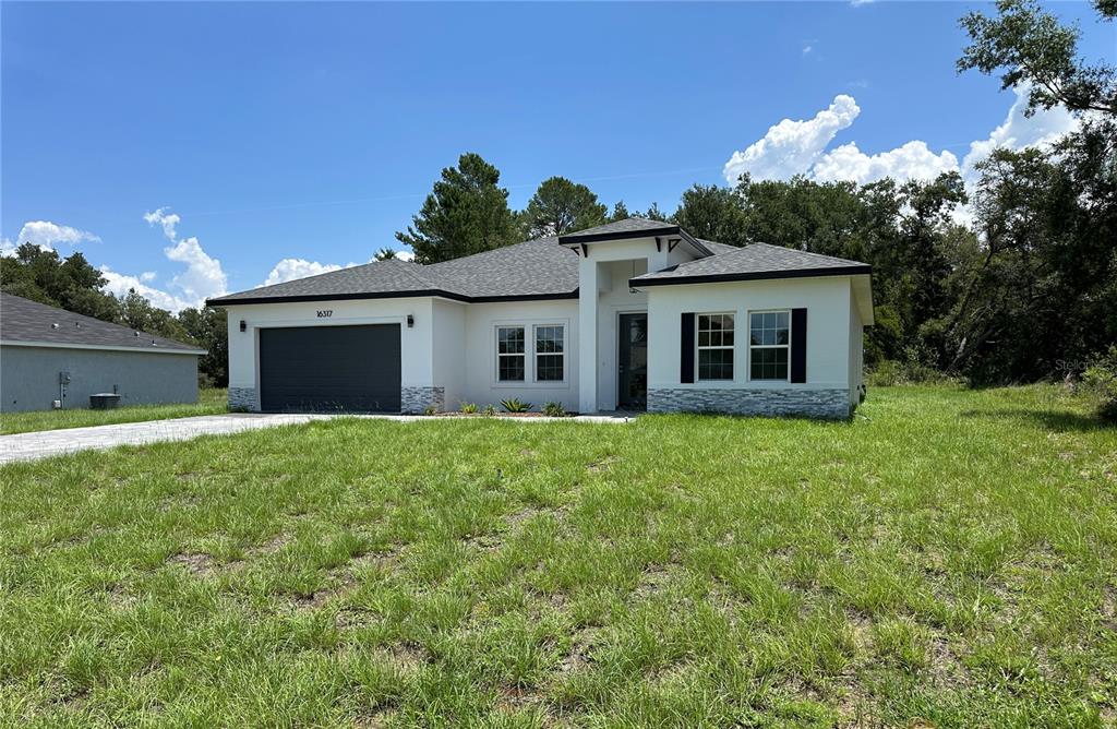 A single-story house with a white stucco exterior, dark garage door, and stone accents — 16317 SW 23RD COURT ROAD, OCALA, FL