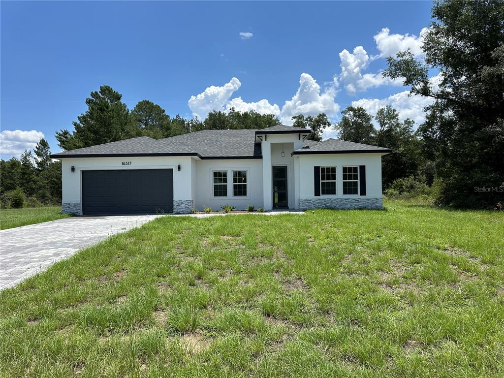 A single-story house with a white exterior, dark garage door, and stone accents — 16317 SW 23RD COURT ROAD, OCALA, FL