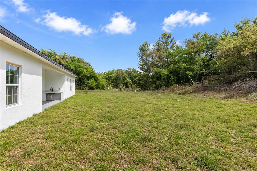 A white house exterior features a covered patio area overlooking a large, grassy backyard — 16317 SW 23RD COURT ROAD, OCALA, FL