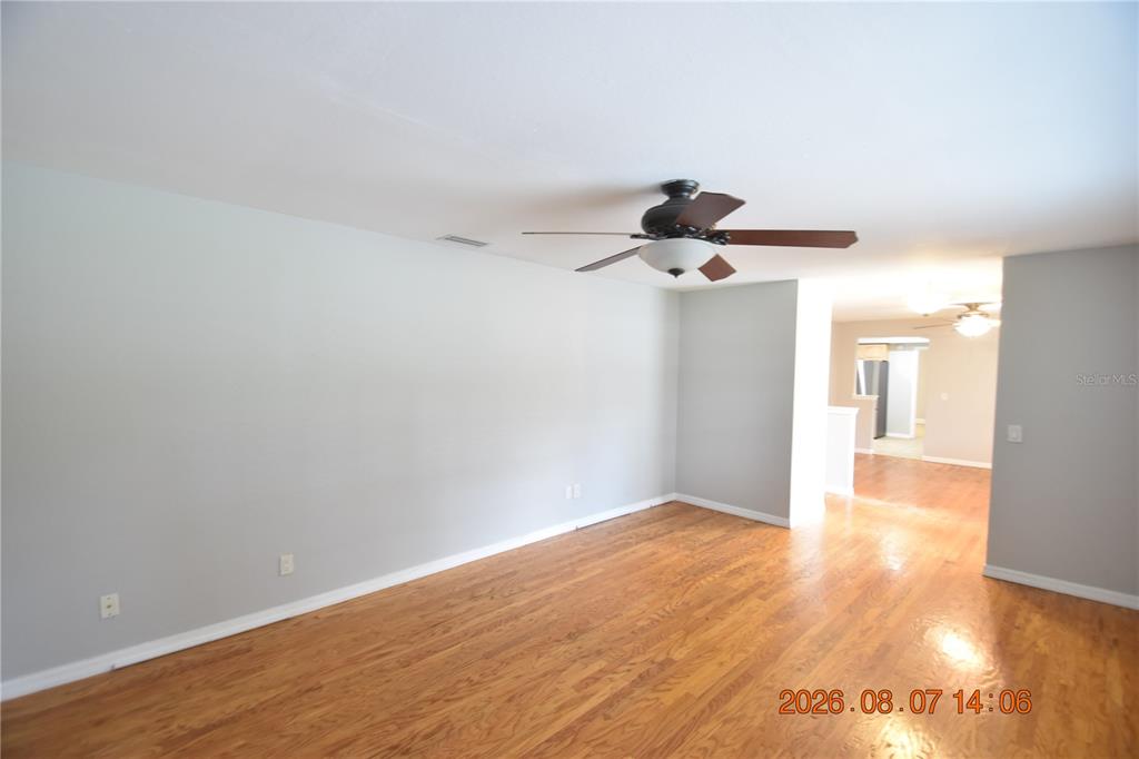 An empty living room features light gray walls, hardwood flooring, and a ceiling fan — 3827 FROSTWOOD COURT, LAND O LAKES, FL