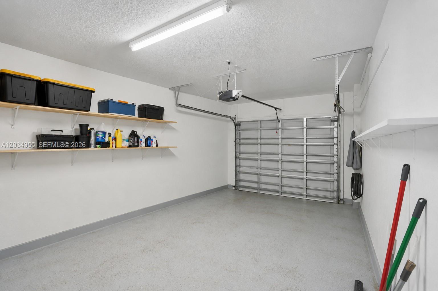 A garage features white walls, a concrete floor, open shelving, and a metal door — 8964 NW 53rd Ct, Sunrise FL 33351, SUNRISE, FL