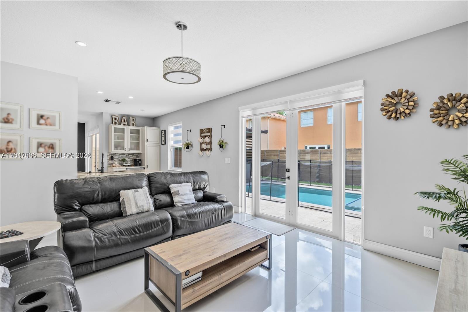 A living room features a dark leather sofa, wood coffee table, and sliding glass doors — 15877 SW 61st Way, Miami FL 33193, MIAMI, FL