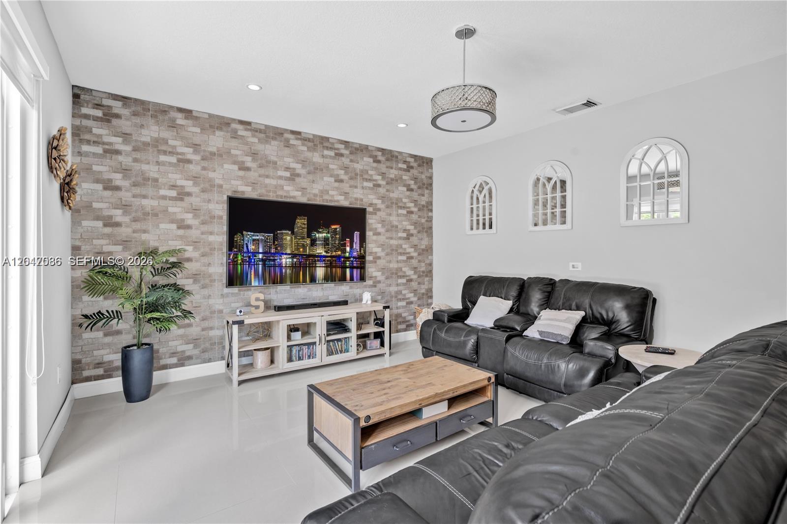 A living room features a brick accent wall, a television, and dark leather furniture — 15877 SW 61st Way, Miami FL 33193, MIAMI, FL