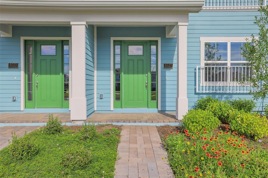 Two green front doors with sidelights on a light blue house with a brick walkway — 6527 TRAILBLAZE BEND, ST CLOUD, FL