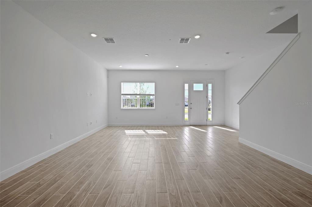 An empty living room features white walls, light wood-look tile flooring, and a front door — 6527 TRAILBLAZE BEND, ST CLOUD, FL