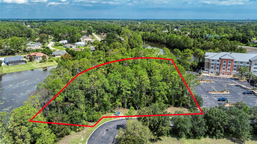 An aerial view shows a wooded lot outlined in red next to a hotel and pond — xxx GARDEN STREET N, PALM COAST, FL